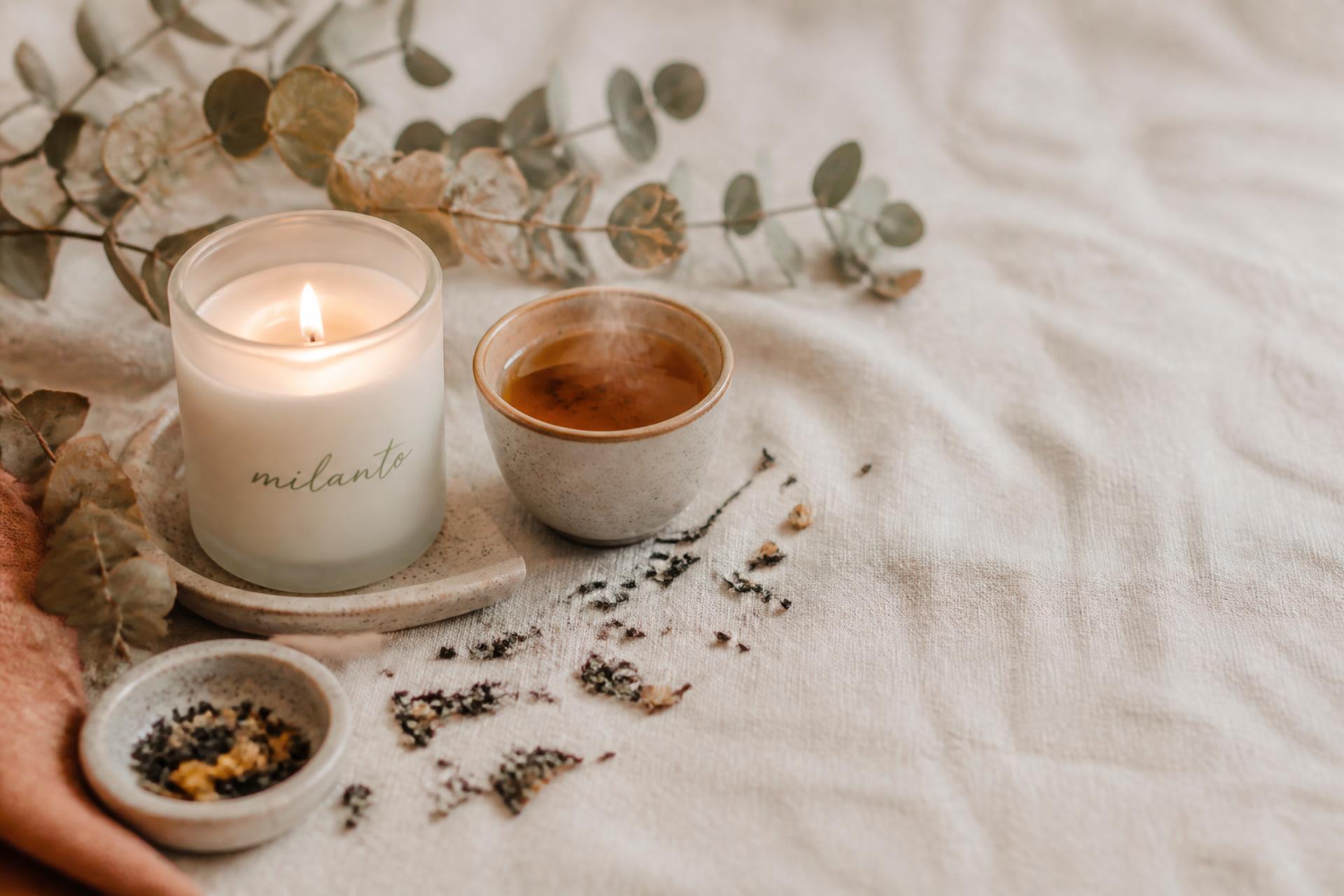 A lit Milanto candle and a cup of tea on soft linen